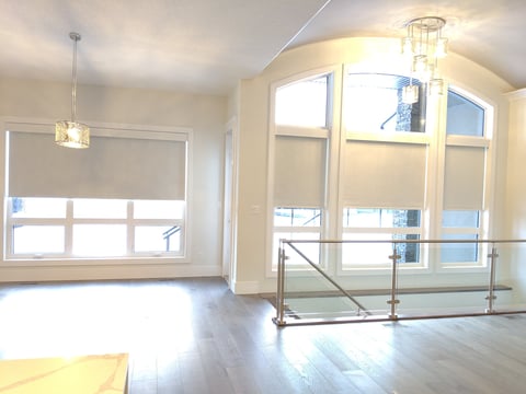Bright modern loft interior with large windows, polished wood floors, pendant light, and metal railing on mezzanine.