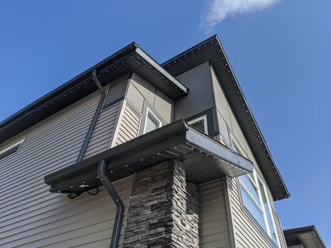 Modern two-story house with white siding, stone chimney, and black roof against clear blue sky