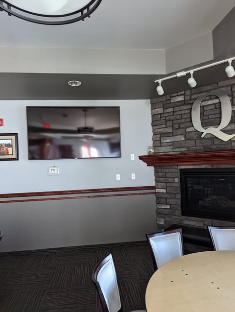 Modern living room with mounted TV, brick fireplace with Q monogram, round table, and two-tone gray walls
