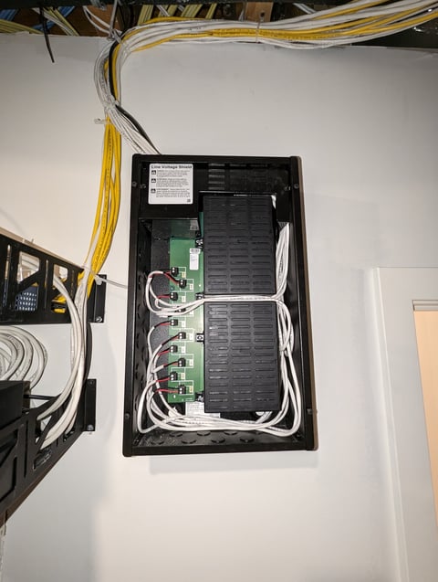 Open electrical panel box mounted on white wall with circuit breakers, green control modules, and yellow and white cables connected