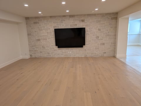 Empty living room with wood flooring, brick feature wall, and flat-screen TV mounted on the wall