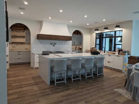 Modern kitchen with large island, stainless steel appliances, white cabinetry, wood flooring, and pendant lighting