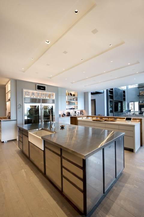Modern kitchen with stainless steel island, white cabinetry, recessed lighting, and blue-tinted glass doors