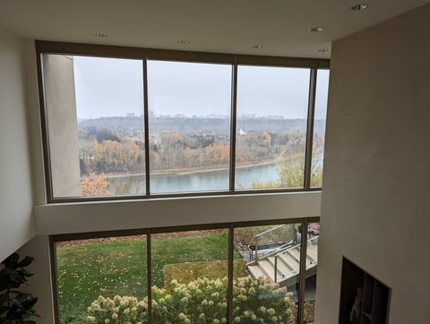 Large windows in a modern room overlooking a river, green lawn, and autumn forest landscape