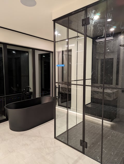 Modern bathroom with black framed glass shower enclosure and freestanding soaking tub against tiled walls