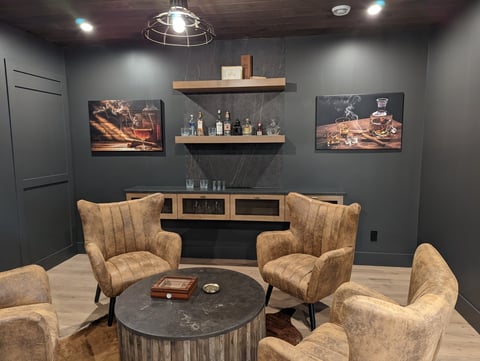 Modern lounge room with tan armchairs, dark marble table, wooden shelves, framed artwork, and industrial ceiling light