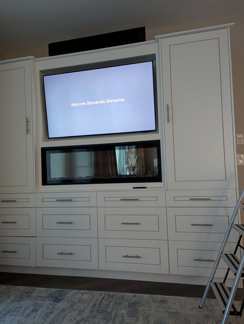Built-in white cabinetry with flat-screen TV displaying welcome message and lower media shelving unit