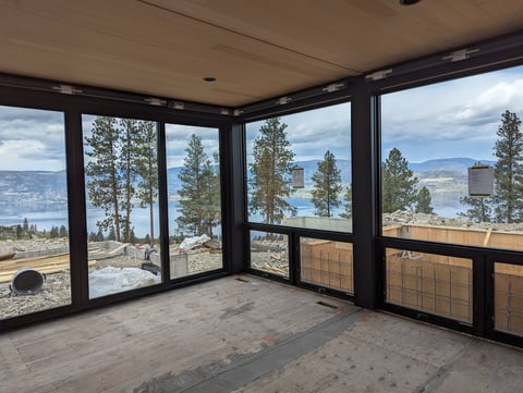 Empty room with floor-to-ceiling windows overlooking a lake, mountains, and forested landscape below