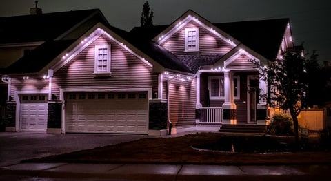 Two-story suburban home illuminated with purple and warm white lighting at night, featuring a two-car garage and front porch.
