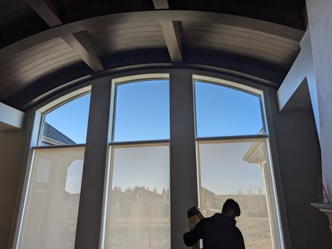 Person silhouetted against large modern windows with arched ceiling and view of forested landscape