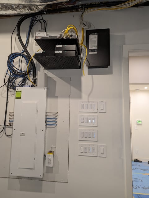 Home electrical panel with network equipment mounted on wall, showing multiple cable connections and light switches below