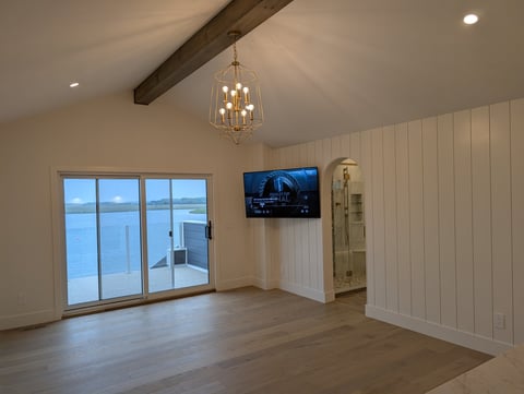 Modern living room with exposed beam ceiling, large glass doors, mounted TV, pendant light fixture, and white shiplap walls