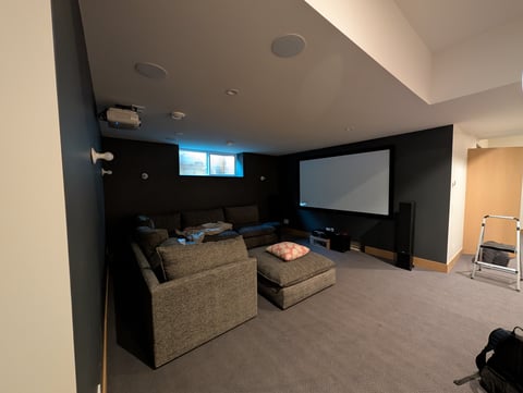 Home theater room with gray carpet, upholstered seating, projection screen, and accent lighting on black walls