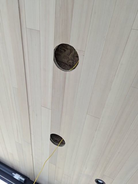 Ceiling with light gray wood paneling showing two dark round recessed lights and a yellow wire or cable.